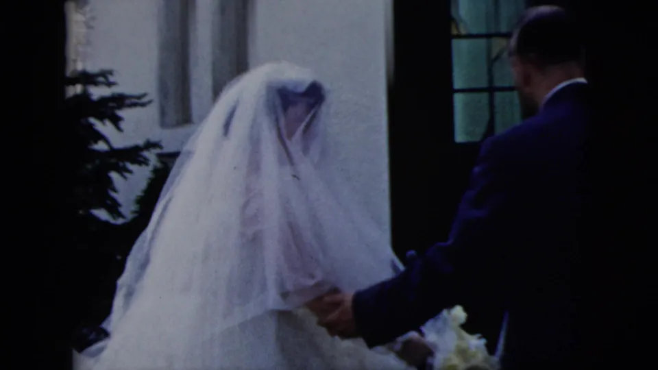 A man in a dark suit appears to guide the veiled bride toward a church entrance in the 1958 New York City wedding scene.