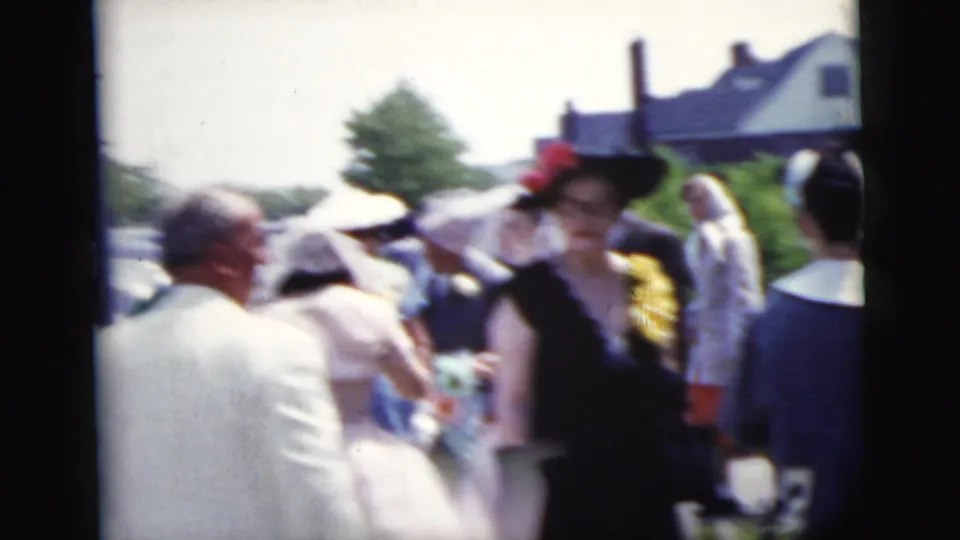 Guests in formal 1950s attire, including women in hats and men in suits, gather outside near the bride and attendants in New York City.