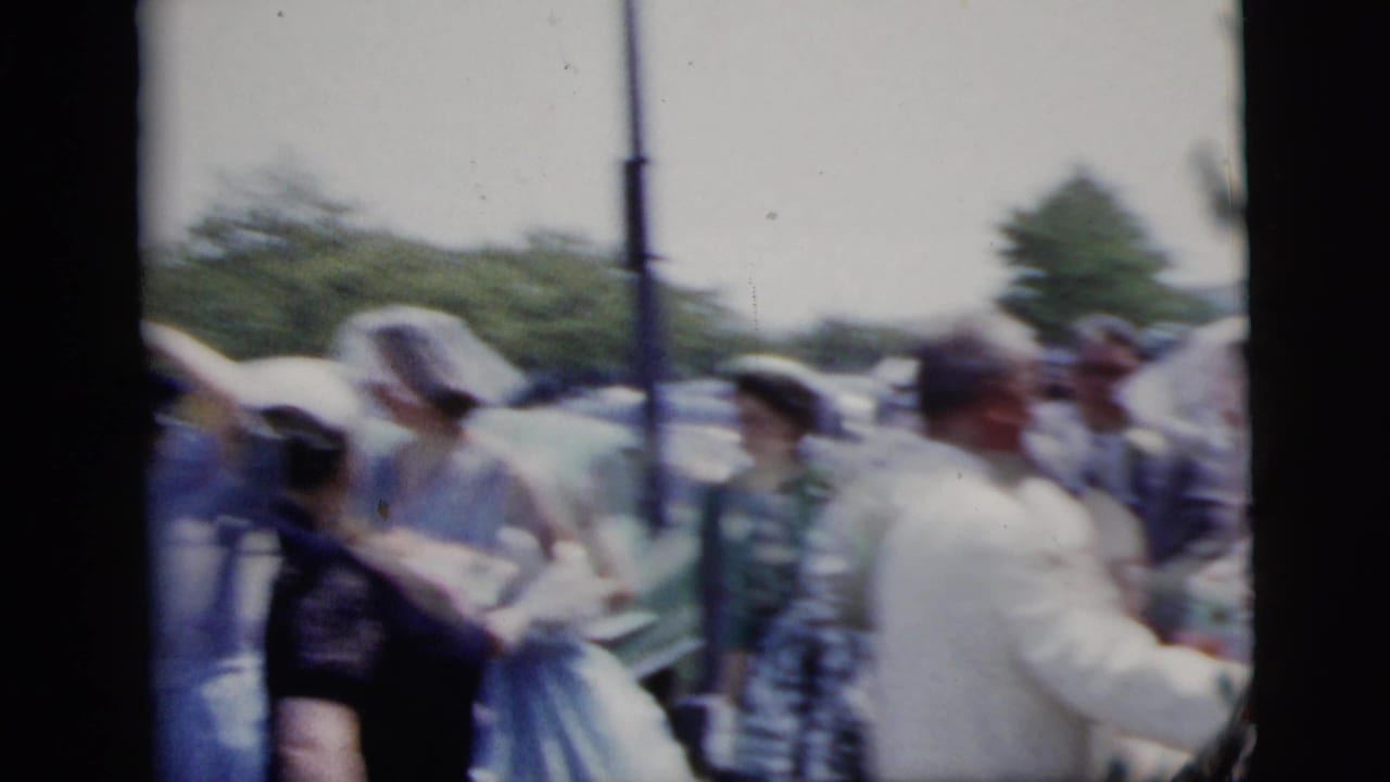 1958 New York City home-movie frame showing a bride and groom among guests during an outdoor wedding moment.