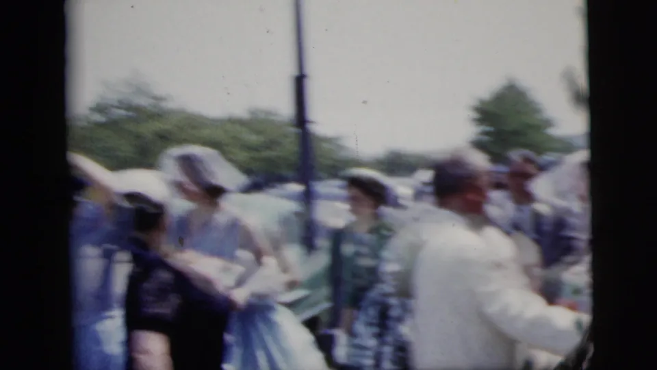 1958 New York City home-movie frame showing a bride and groom among guests during an outdoor wedding moment.