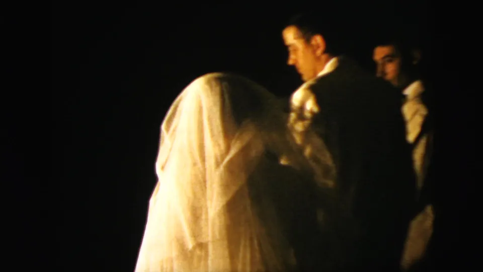 Bride viewed from behind during a 1958 New York City wedding ceremony, with groom and guests nearby in low light.