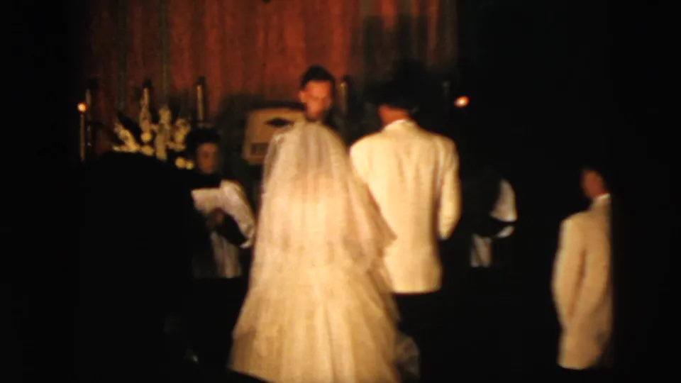 1958 New York City home-movie frame showing the bride and groom from behind as they kneel during a church wedding ceremony.