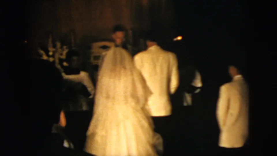 Soft 8mm frame from a 1958 New York City wedding, with the bride and groom kneeling near the altar as clergy and attendants stand nearby.