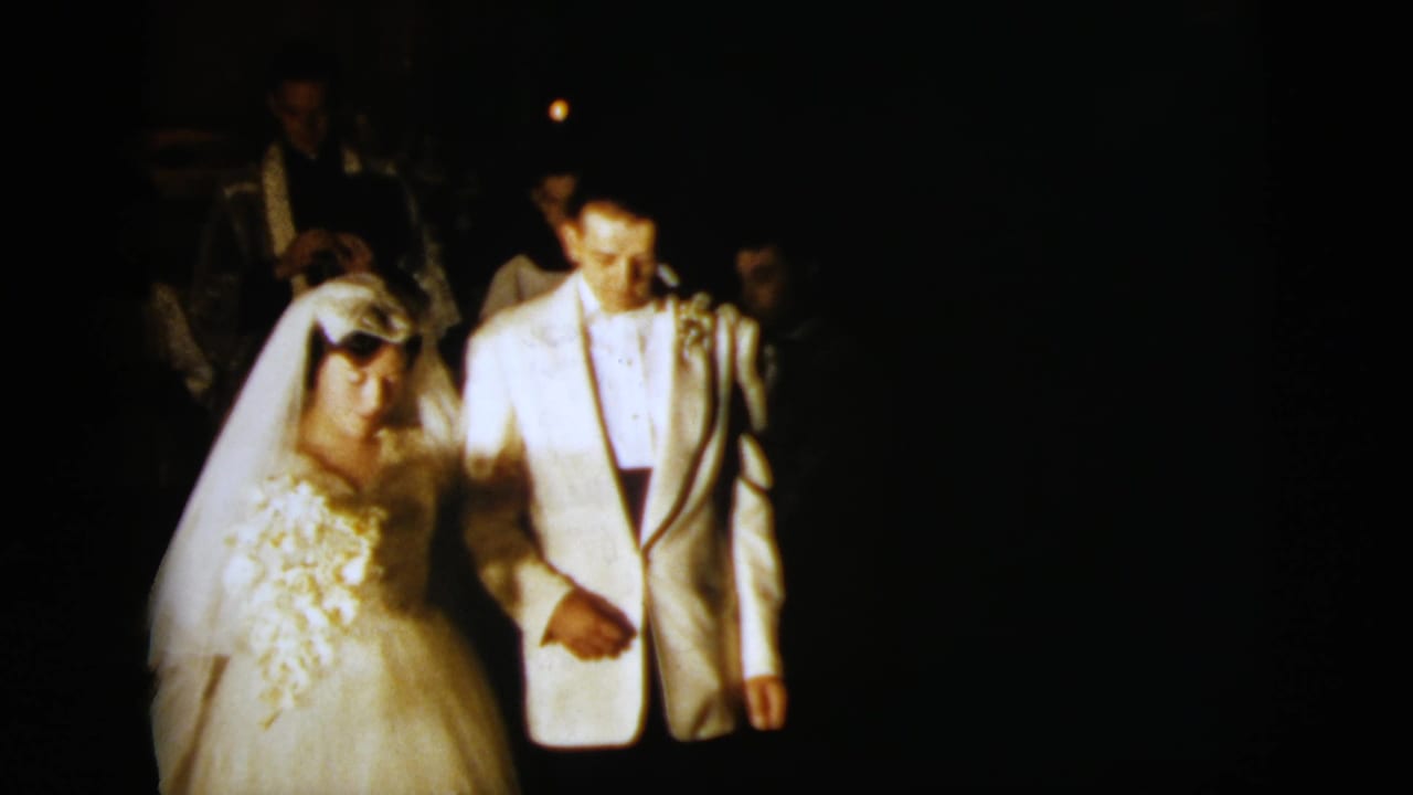 Bride and groom walk arm-in-arm at night with guests behind them.