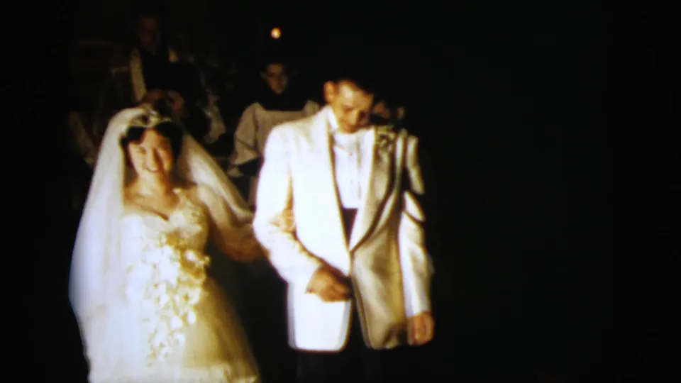 The bride smiles in her wedding gown and veil as the groom walks beside her, both framed by dark 8mm nighttime footage.