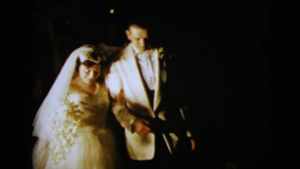 The newlyweds walk close together at night, with the bride's veil and gown and the groom's light tuxedo prominent in the frame.