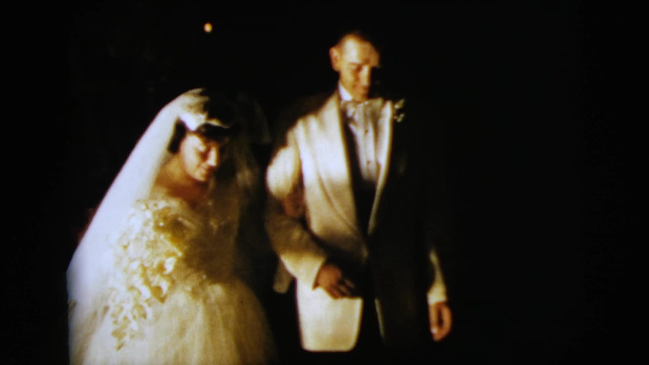 Bride in a white gown and veil walks beside a groom in a white jacket at night.
