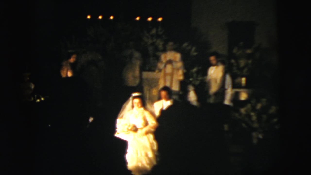 1958 New York City wedding footage showing the bride and groom walking in a dark church with candles and floral decoration visible.