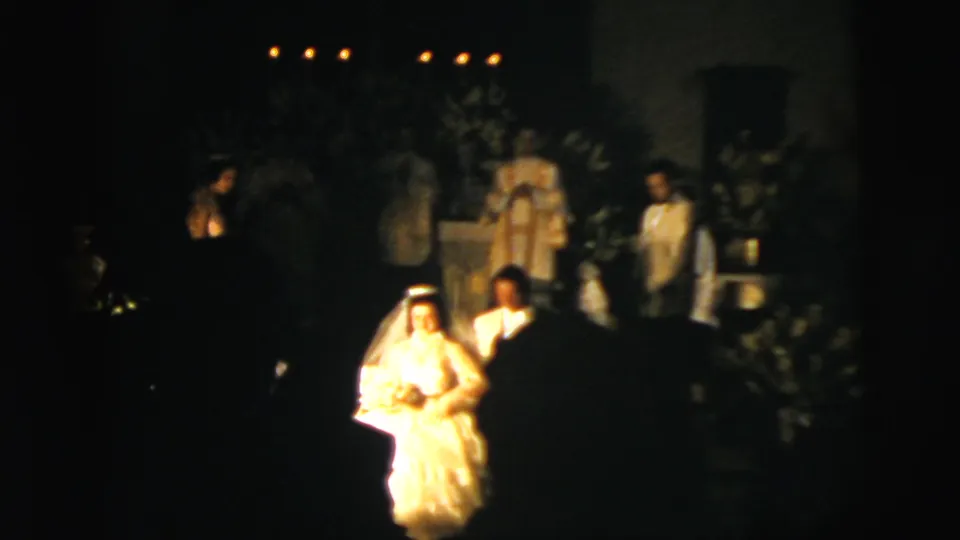 1958 New York City wedding footage showing the bride and groom walking in a dark church with candles and floral decoration visible.