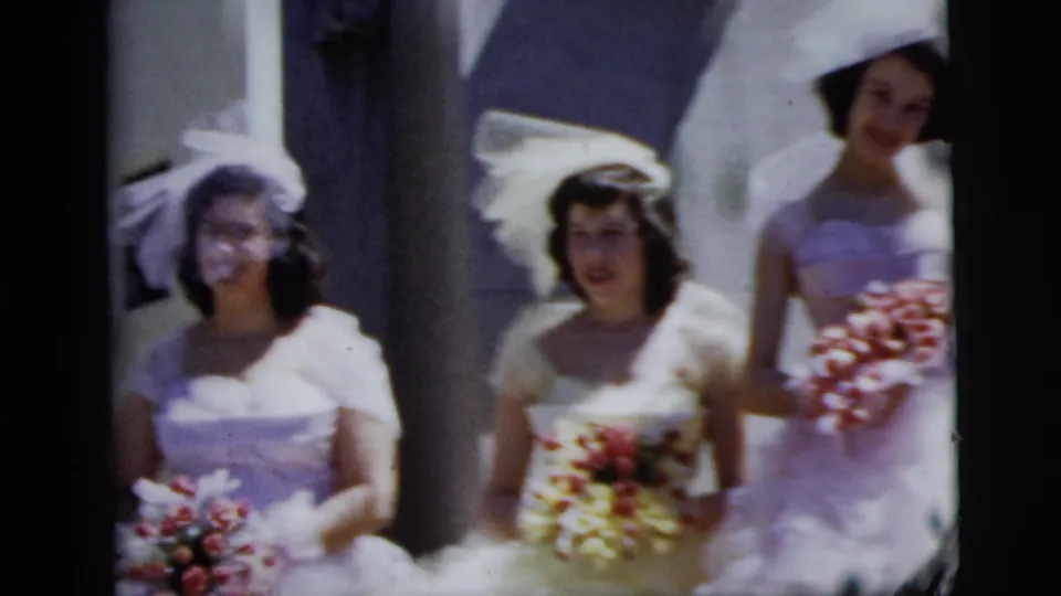1958 New York City wedding frame showing three bridesmaids or attendants in white dresses holding flower bouquets after the church ceremony.