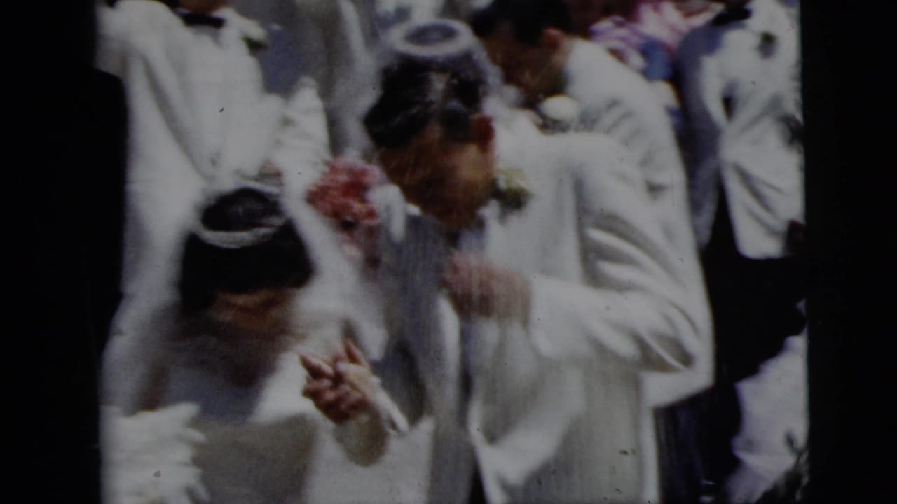 1958 New York City home-movie frame of a bride and groom moving through guests during a rice-throwing wedding exit.