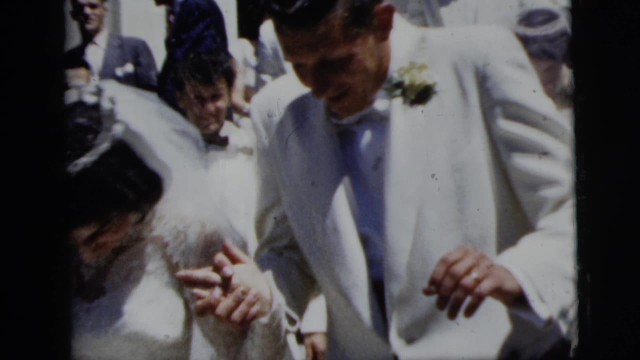 The bride and groom appear hand in hand in a 1958 New York City wedding crowd, with rice visible near their clothing.