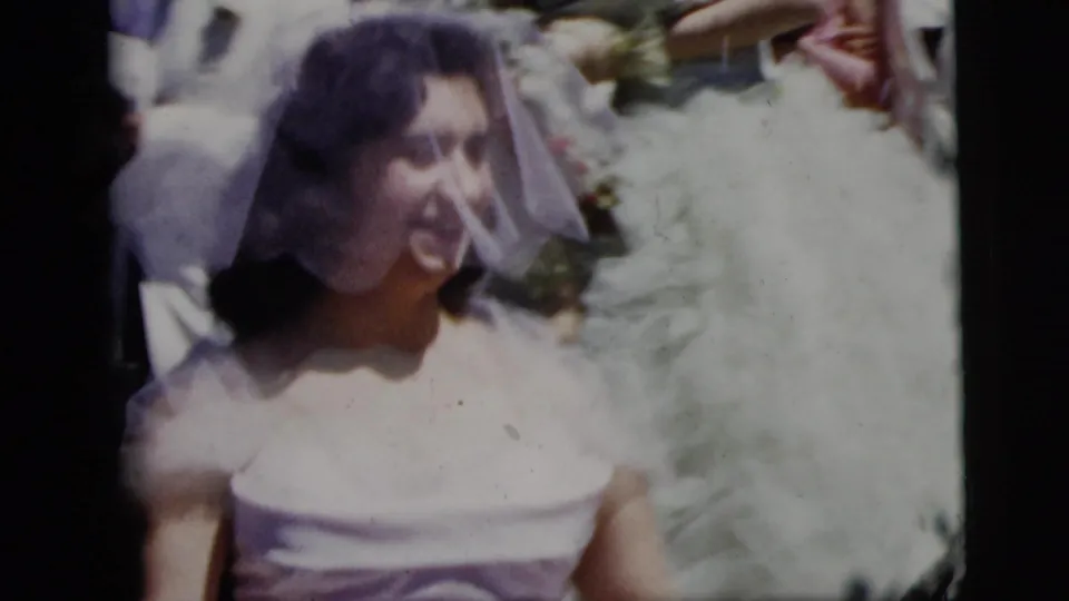 Close 1958 New York City home-movie view of a smiling bride in a white veil with guests and flowers nearby.