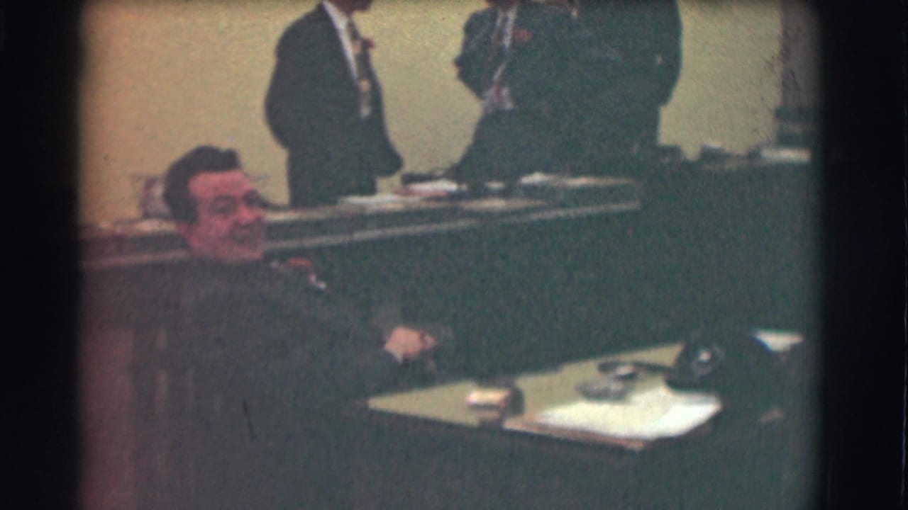 Saint Louis 1959 office footage shows a seated man smiling toward the camera with suited men standing behind a long desk.