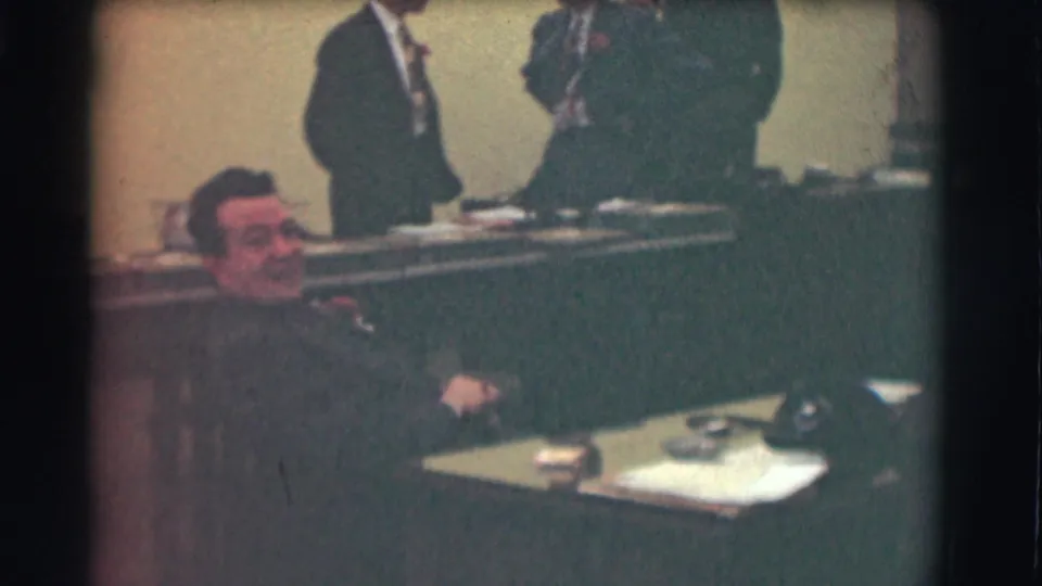 Saint Louis 1959 office footage shows a seated man smiling toward the camera with suited men standing behind a long desk.