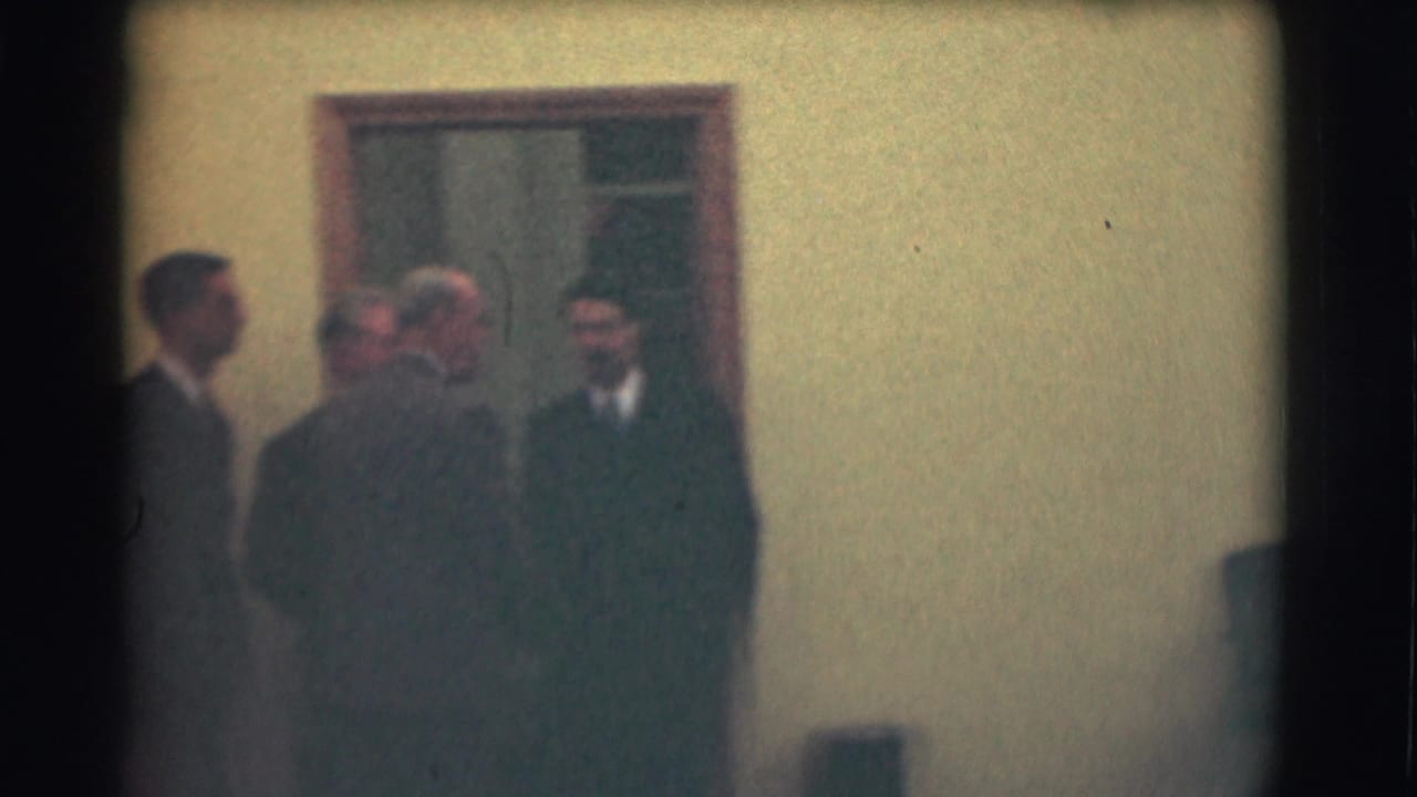 A small group of suited men stands outside near a doorway.