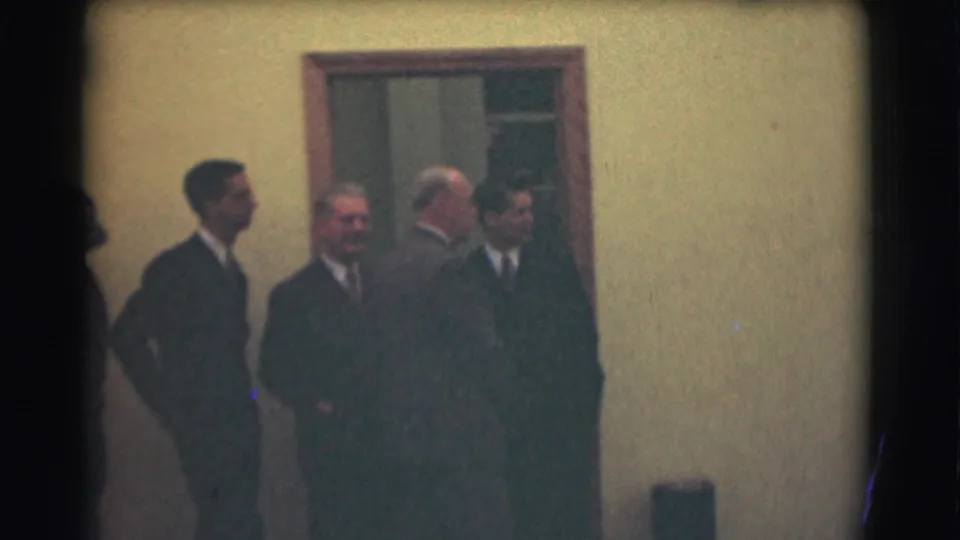 Four formally dressed men stand by a doorway in the 1959 Saint Louis home-movie footage, facing different directions as they wait.