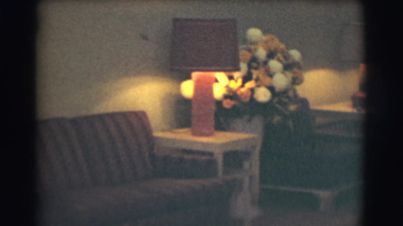 A dimly lit formal interior shows a striped couch, side table, warm table lamp, and large floral arrangement, matching the funeral-home lobby context supplied by the metadata.