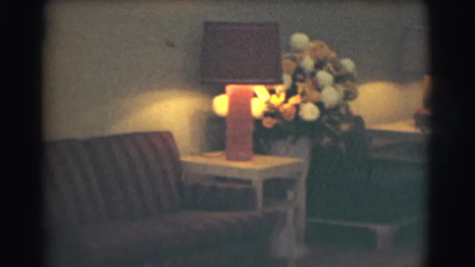 A dimly lit formal interior shows a striped couch, side table, warm table lamp, and large floral arrangement, matching the funeral-home lobby context supplied by the metadata.