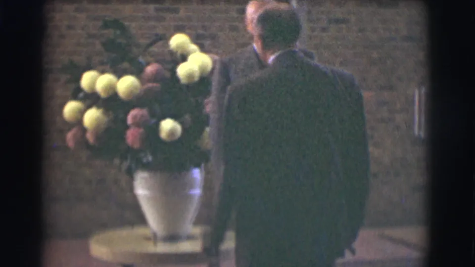 A suited man is seen from behind near the floral arrangement, suggesting quiet movement inside the Saint Louis church interior.