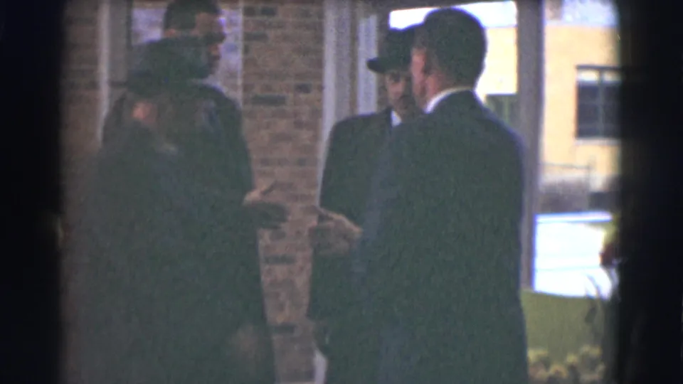 A small group of men in suits, coats, and hats converse near the entryway during a Saint Louis memorial gathering.