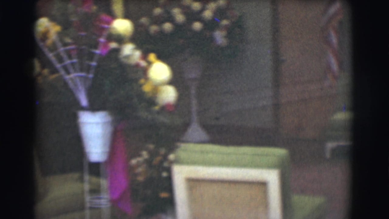 1959 Saint Louis 8mm frame showing yellow and pink floral arrangements in white vases near an interior doorway and wall, with soft focus and dark frame edges.