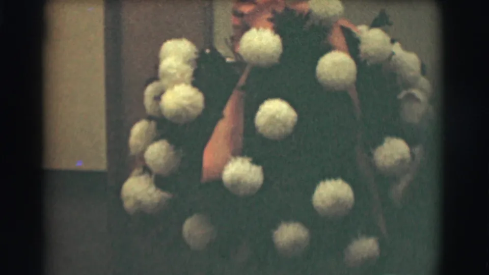 A man in a dark suit and tie appears beside a large pale floral arrangement in this 1959 Saint Louis home-movie frame.