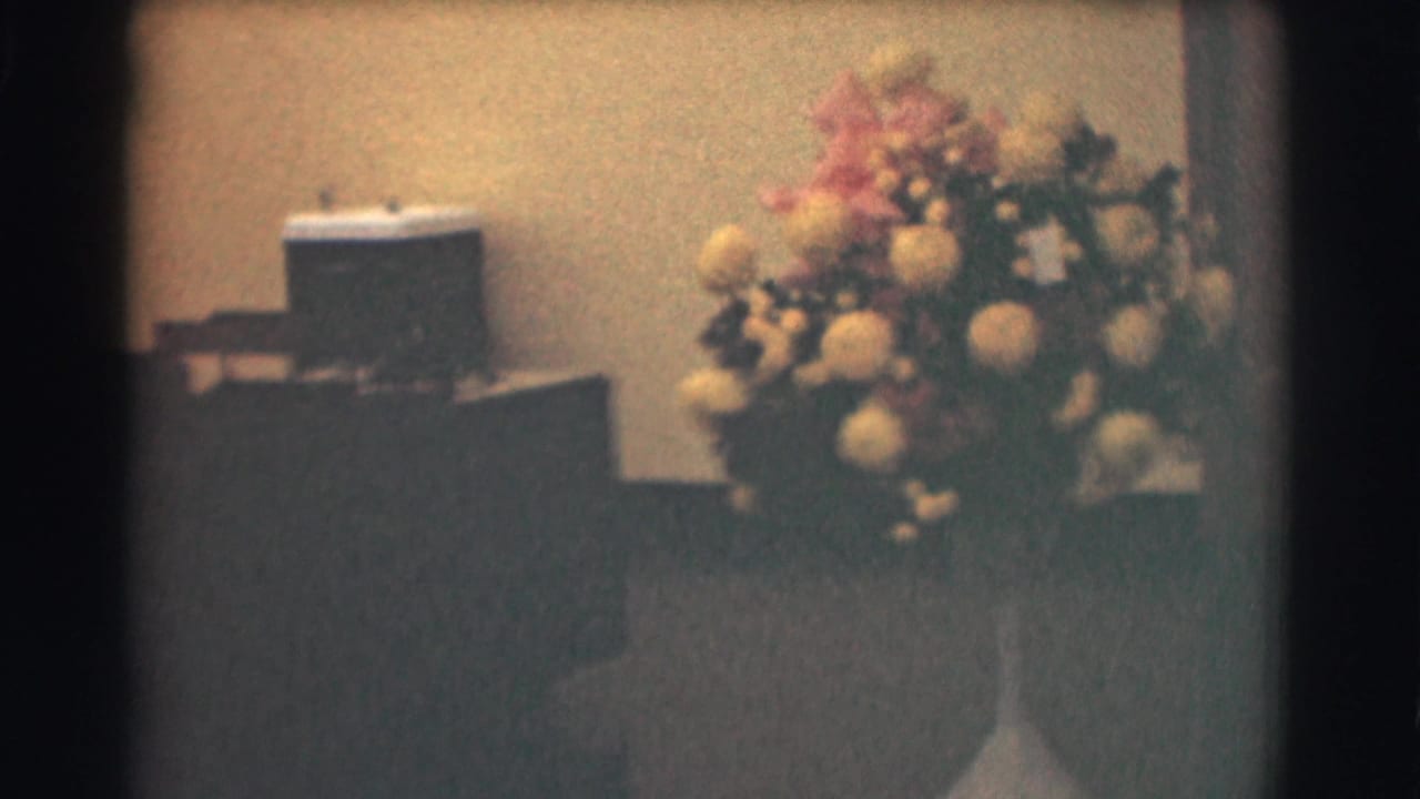 Office interior with floral arrangement, desk furniture, and a small water cooler against a plain wall.