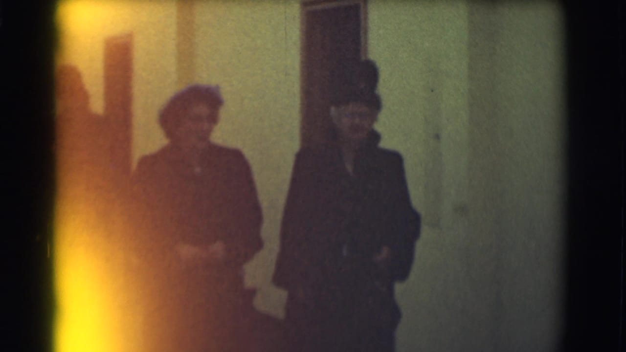 Two women in dark coats and hats walk beside a man in a suit.