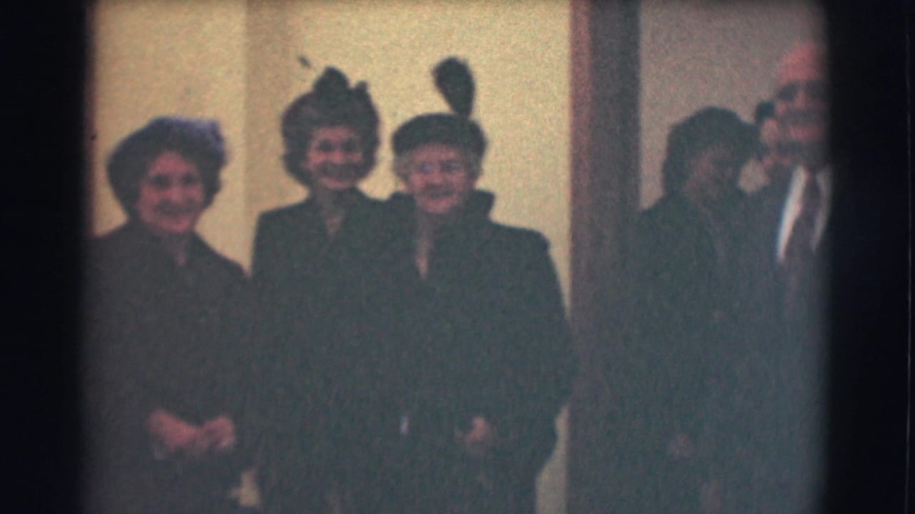 1959 Saint Louis home-movie frame with three elderly women in dress hats and dark coats posing indoors, with another adult partly visible at right.