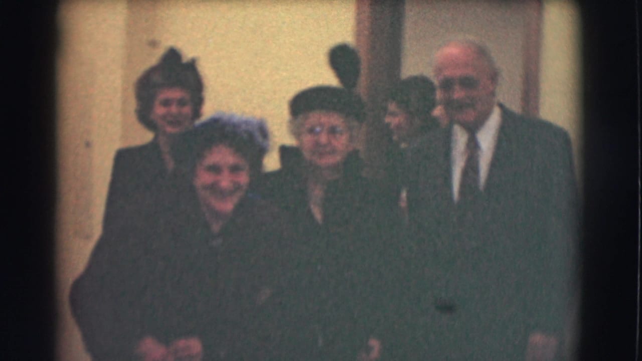 The group faces the camera outside a Saint Louis building, with older women in dark coats and hats and a suited man at the right.