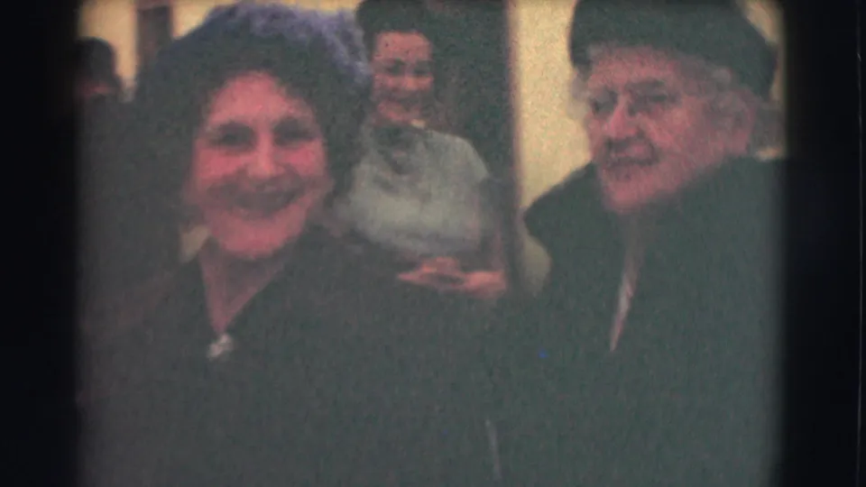 A smiling woman and an older woman in a formal hat appear close to the camera in 1959 Saint Louis footage near a building entrance.