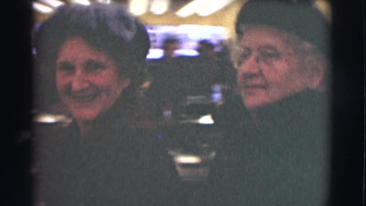 Two older women smiling close to the camera in a softly lit interior.