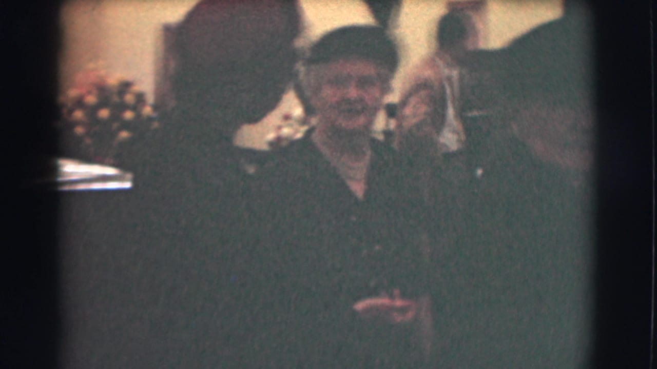 A woman wearing a dark hat and dress faces the camera among other dressed adults.