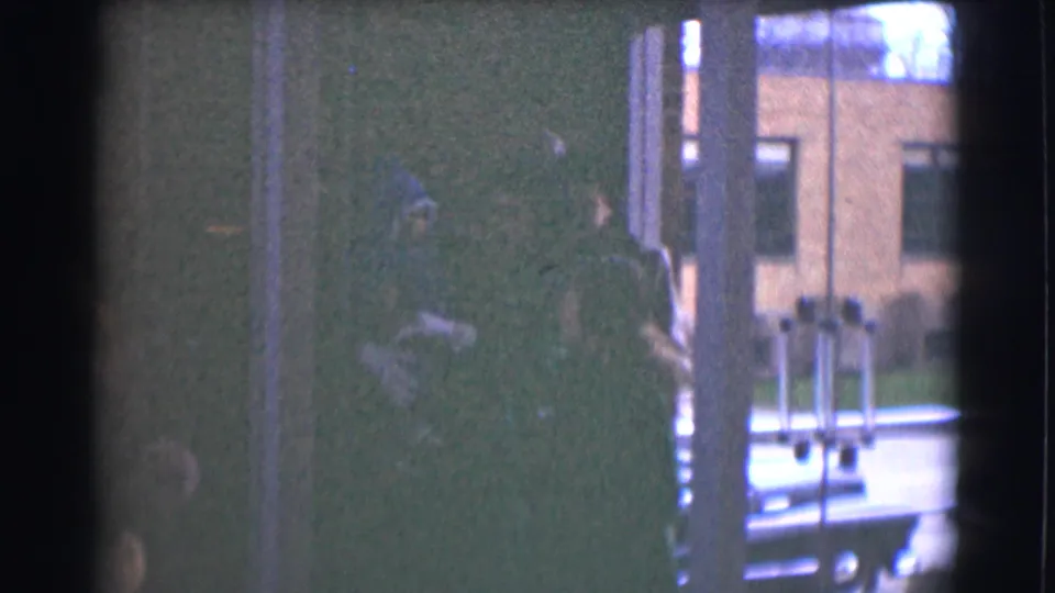 The final frame shows adults near glass inside a private or semi-private space, with a building facade visible outside in soft 8mm color.