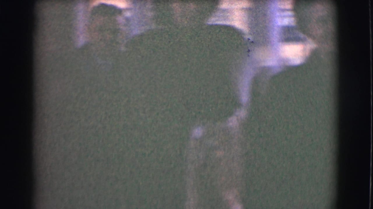 Low-exposure 1959 St. Louis home-movie frame with indistinct outdoor figures and soft winter clothing shapes.