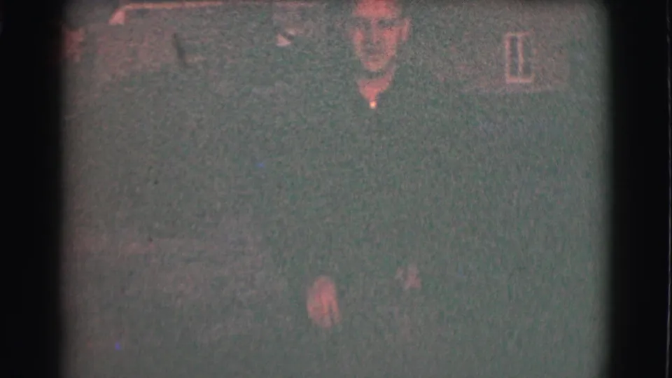 Grainy 1959 St. Louis frame showing an adult in dark winter clothing within a dim residential outdoor setting.
