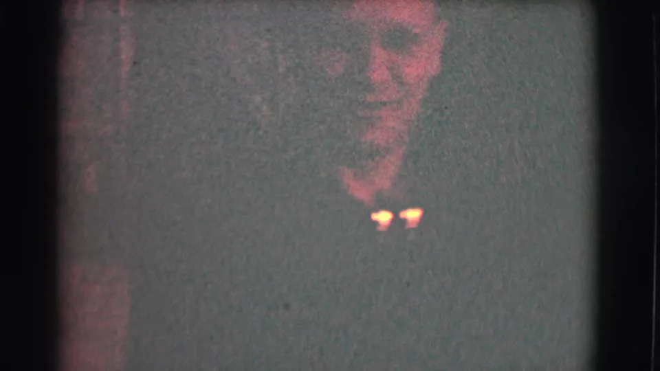 In this 1959 Saint Louis 8mm frame, a man with glasses appears near the top of a dim room, partly obscured by grain and low exposure.