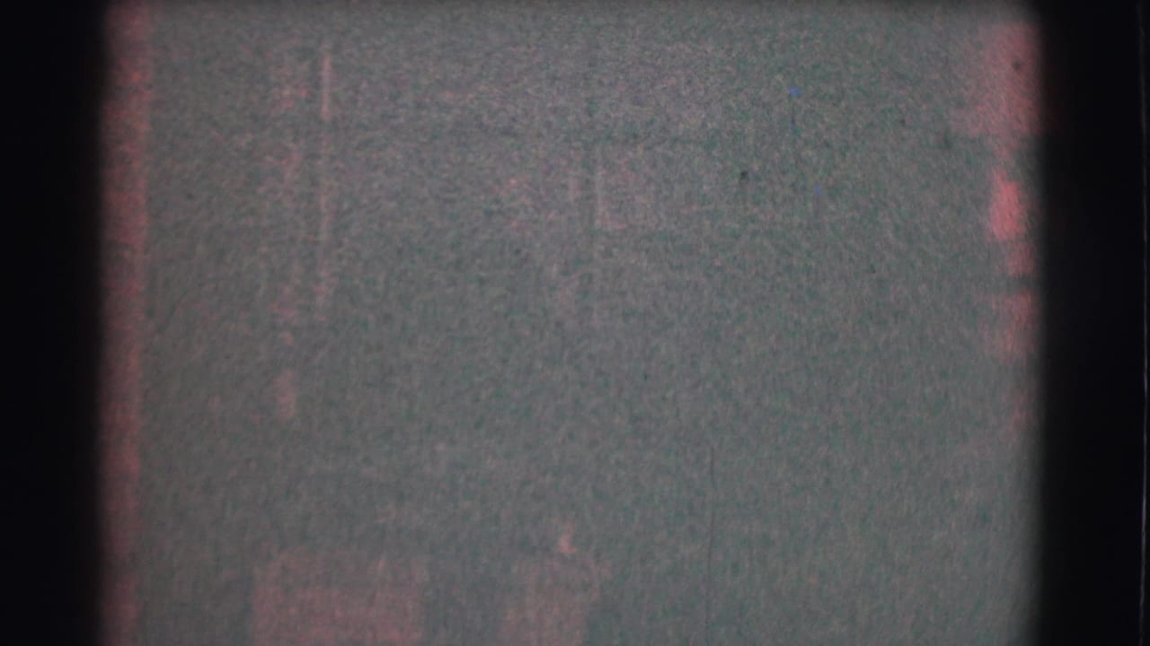 A dim 1959 Saint Louis home-movie frame shows faint interior details, reddish film cast, and very little of the subject clearly visible.