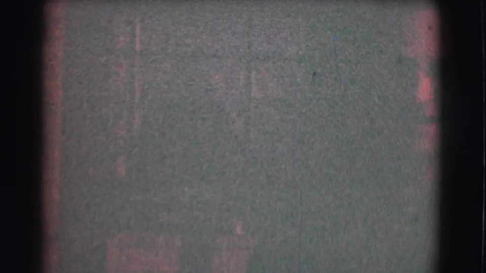 A dim 1959 Saint Louis home-movie frame shows faint interior details, reddish film cast, and very little of the subject clearly visible.