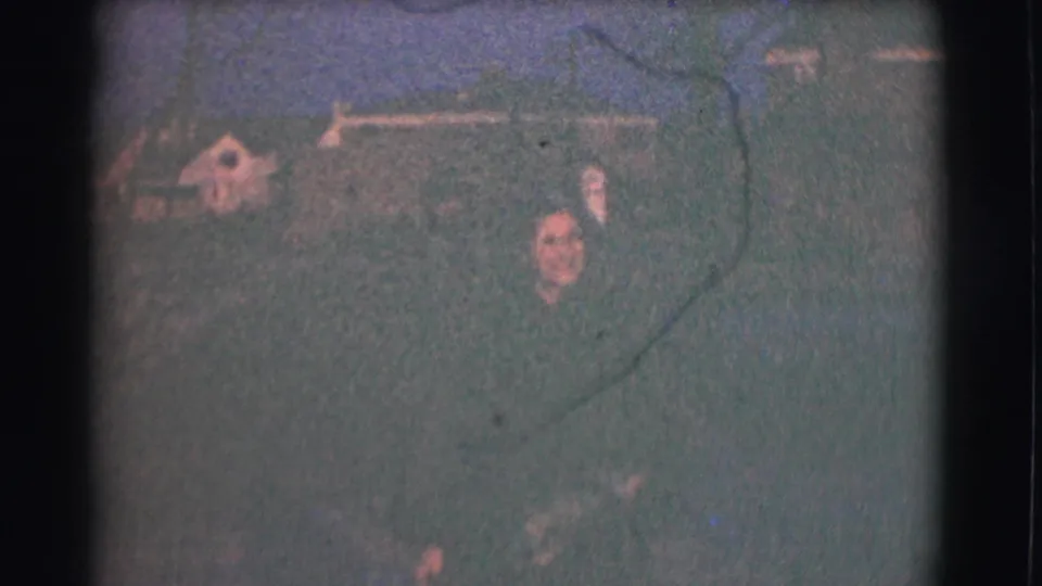 Wide 1959 Saint Louis home-movie frame showing two adults in a residential yard with houses and trees in the background.