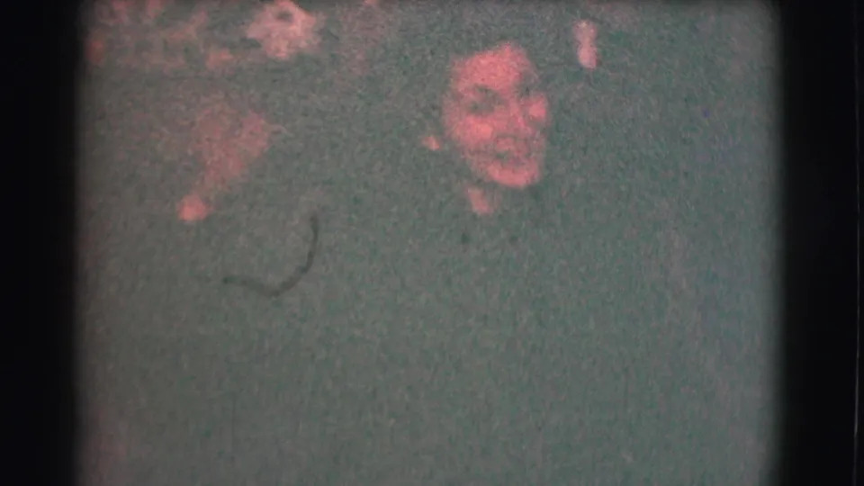 The 1959 8mm frame shows the woman turning slightly at night, with her face and upper body softened by grain, darkness, and handheld exposure.
