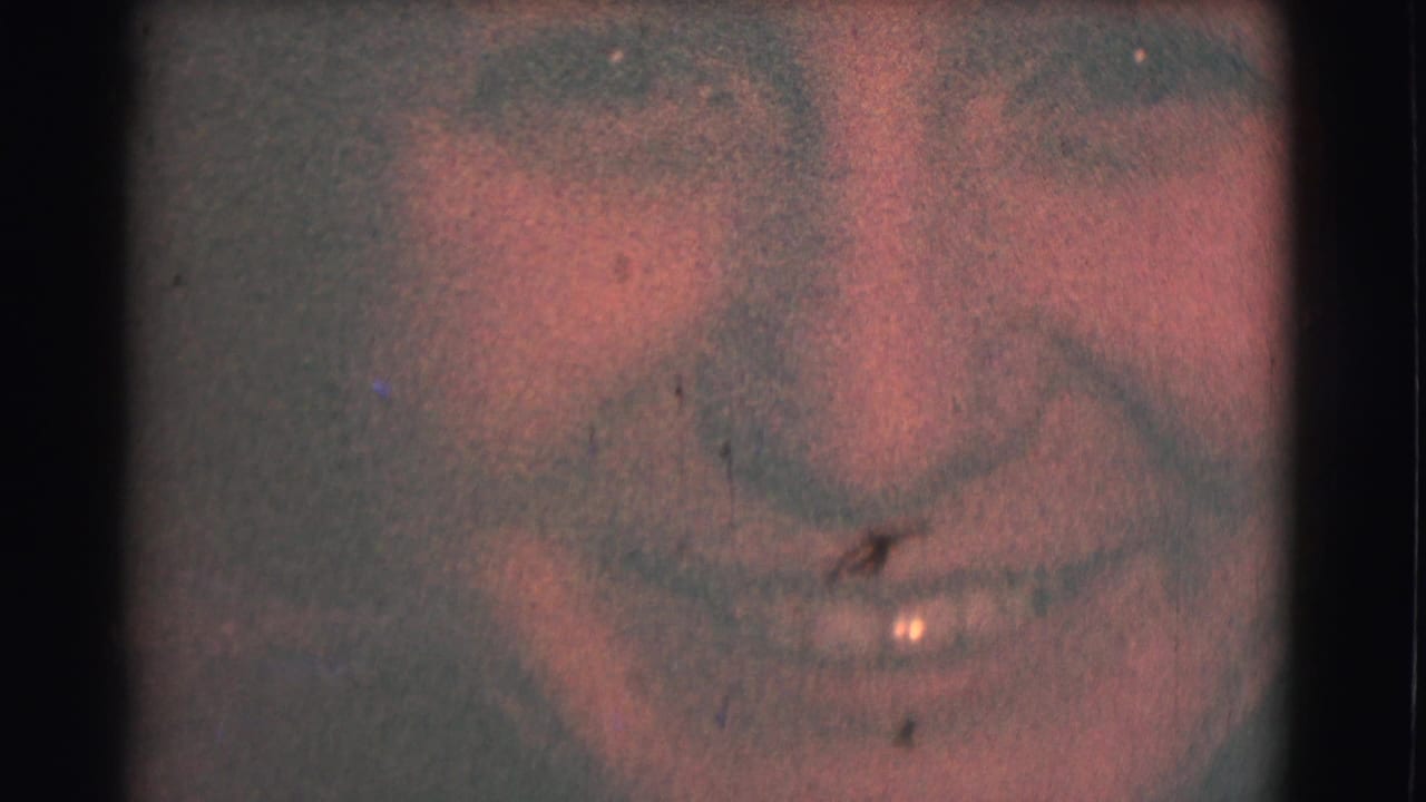 The camera zooms tightly onto the woman's smiling face, with visible 8mm grain, color fading, and gate-edge darkness.