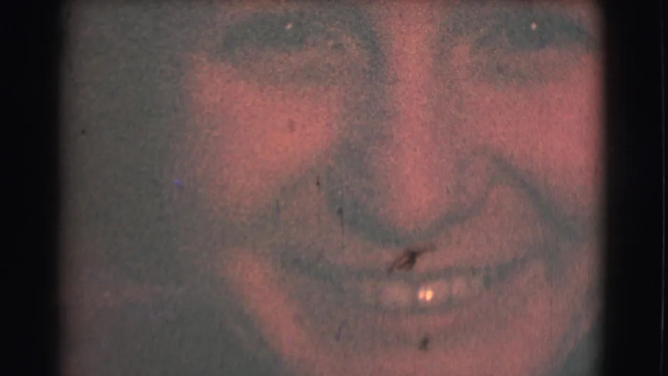 The camera zooms tightly onto the woman's smiling face, with visible 8mm grain, color fading, and gate-edge darkness.