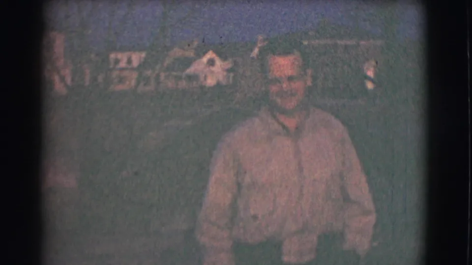 In 1959 Saint Louis home-movie footage, an adult man in a collared shirt smiles while walking toward the camera across a yard.