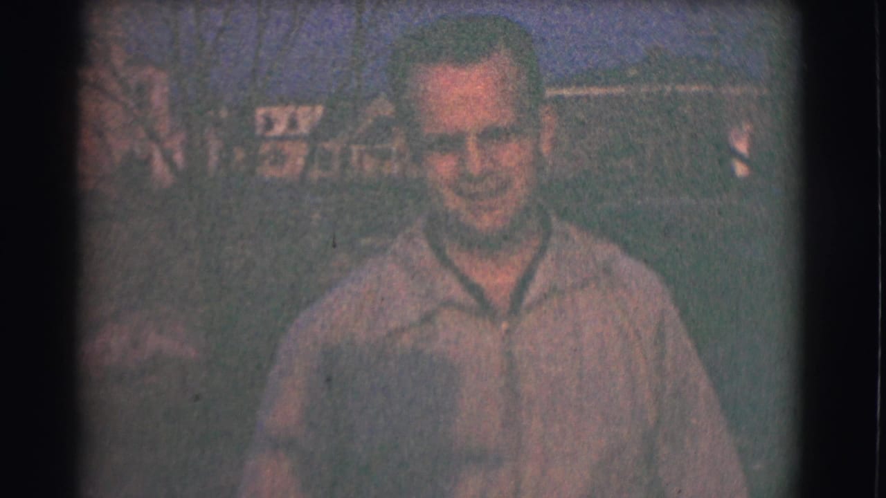 The adult man approaches the camera in the Saint Louis 1959 home movie, his face clearer against a soft outdoor residential background.