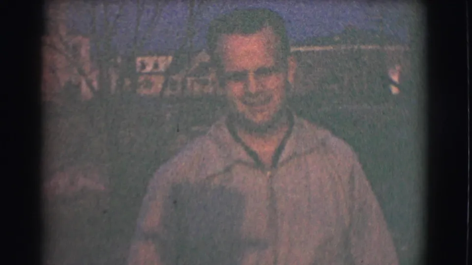 The adult man approaches the camera in the Saint Louis 1959 home movie, his face clearer against a soft outdoor residential background.
