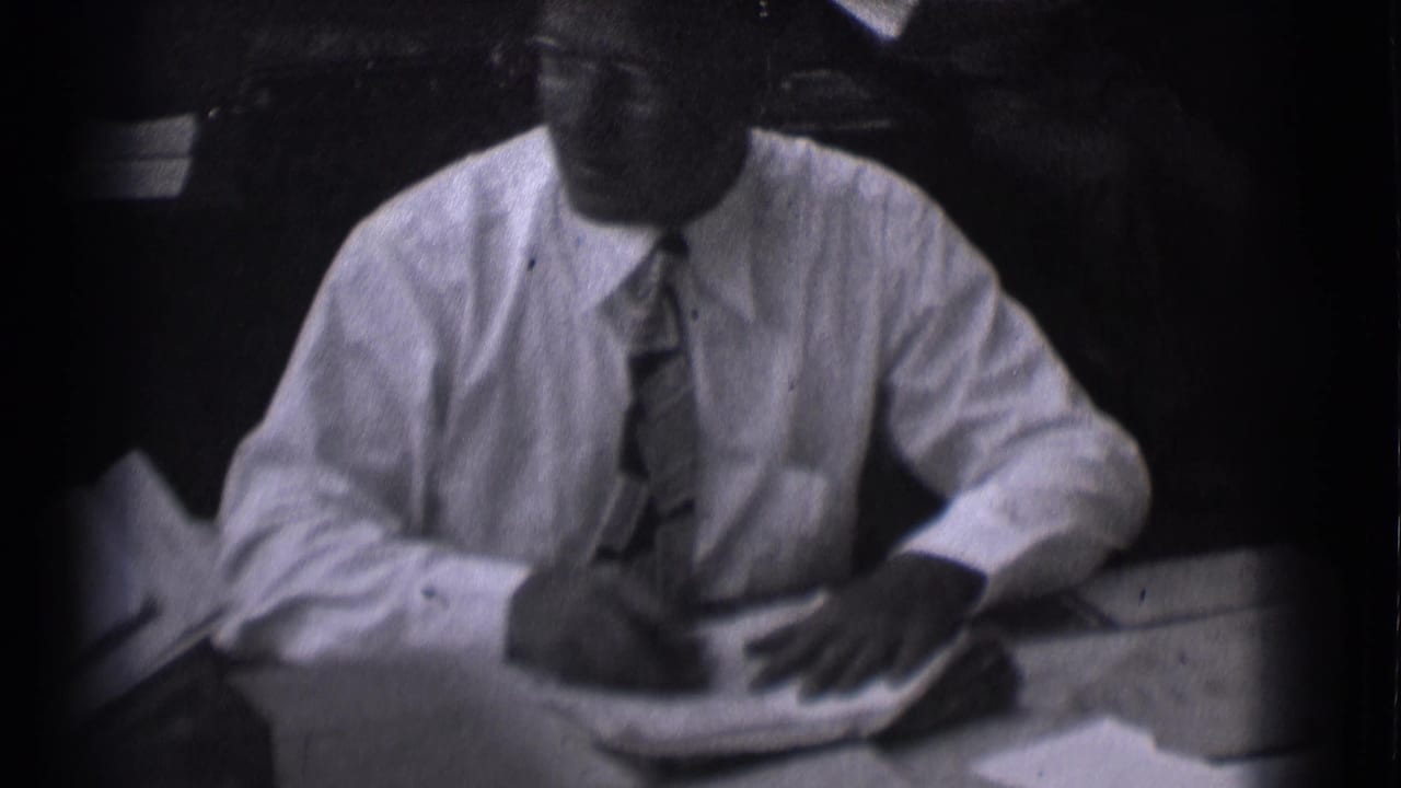 Adult man in a white shirt and patterned tie sits at a desk with papers in Saint Louis, Missouri archival footage.