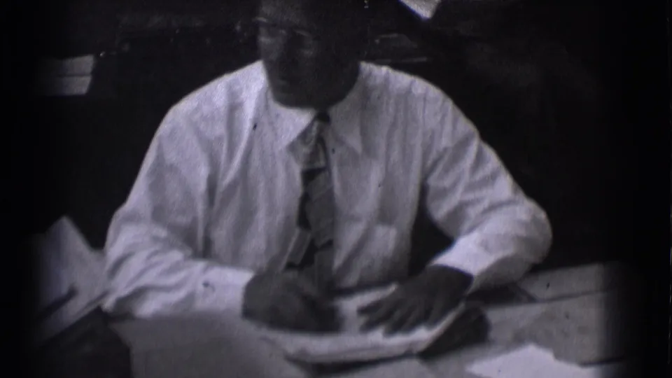 Adult man in a white shirt and patterned tie sits at a desk with papers in Saint Louis, Missouri archival footage.