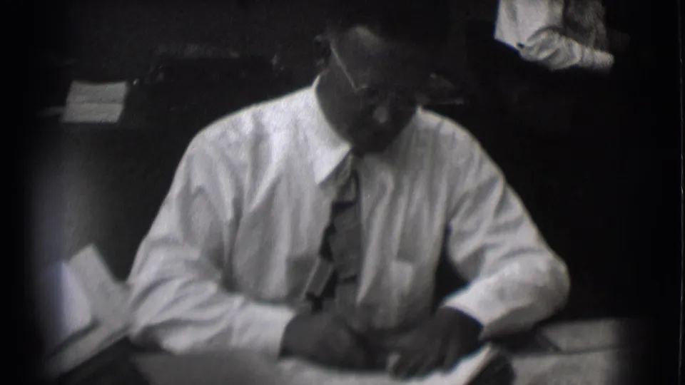 Man in glasses and tie looks down toward desk papers in soft-focus 1959 Saint Louis office footage.
